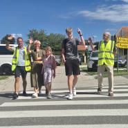 Prostovoljci in ravnateljica spremljajo otroke čez prehod za pešce